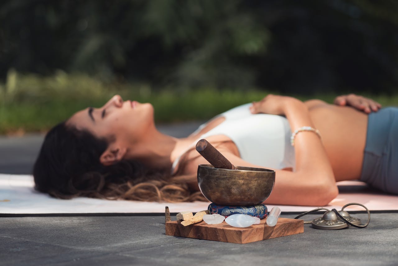 A woman practices relaxation with a singing bowl and crystals in an outdoor setting.